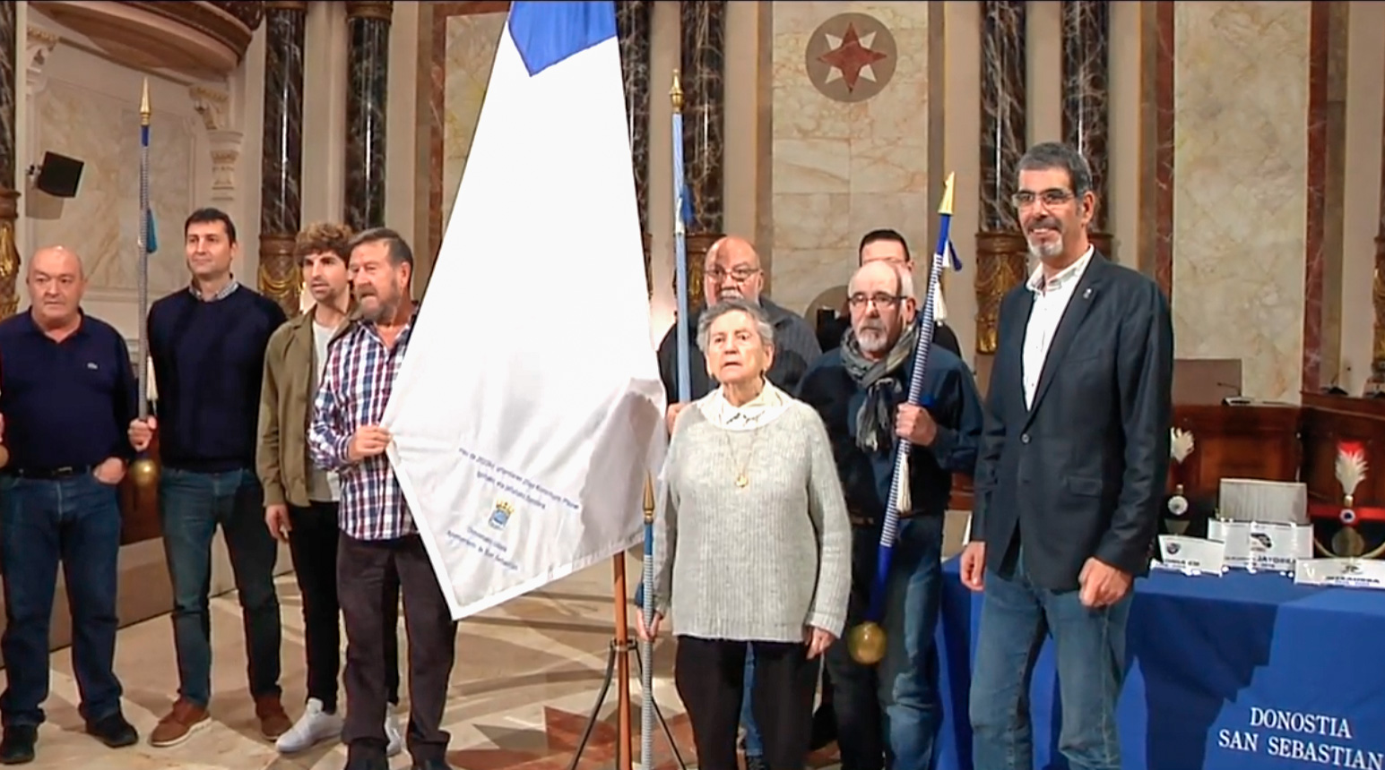 Varias personas reunidas en el ayuntamiento junto a la bandera de San Sebastián
