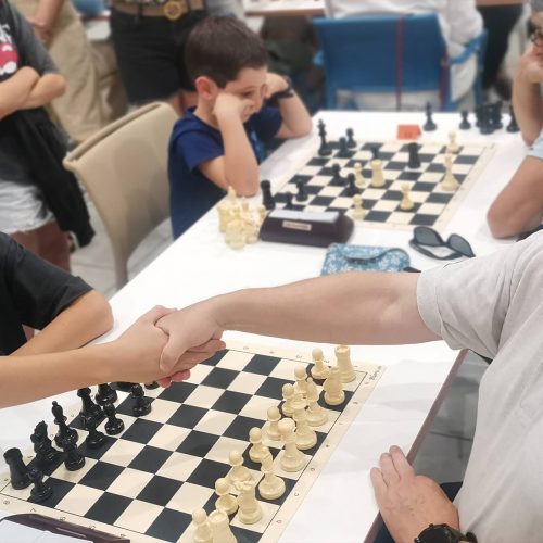 Una persona mayor estrechando la mano a un niño, sentados en una mesa con un juego de ajedrez