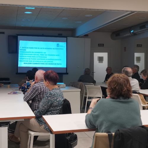 grupo de personas reunido en una sala mirando una pantalla con contenido