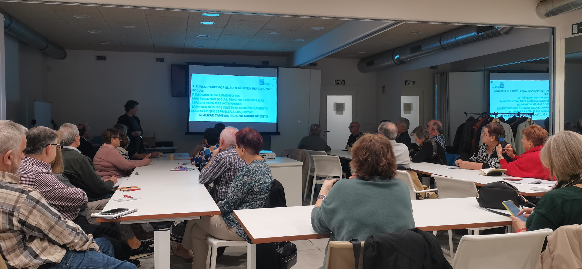 grupo de personas reunido en una sala mirando una pantalla con contenido