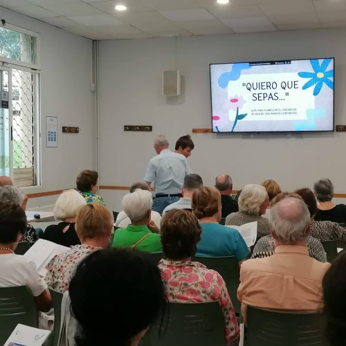 grupo de personas reunido en una sala mirando una pantalla con contenido