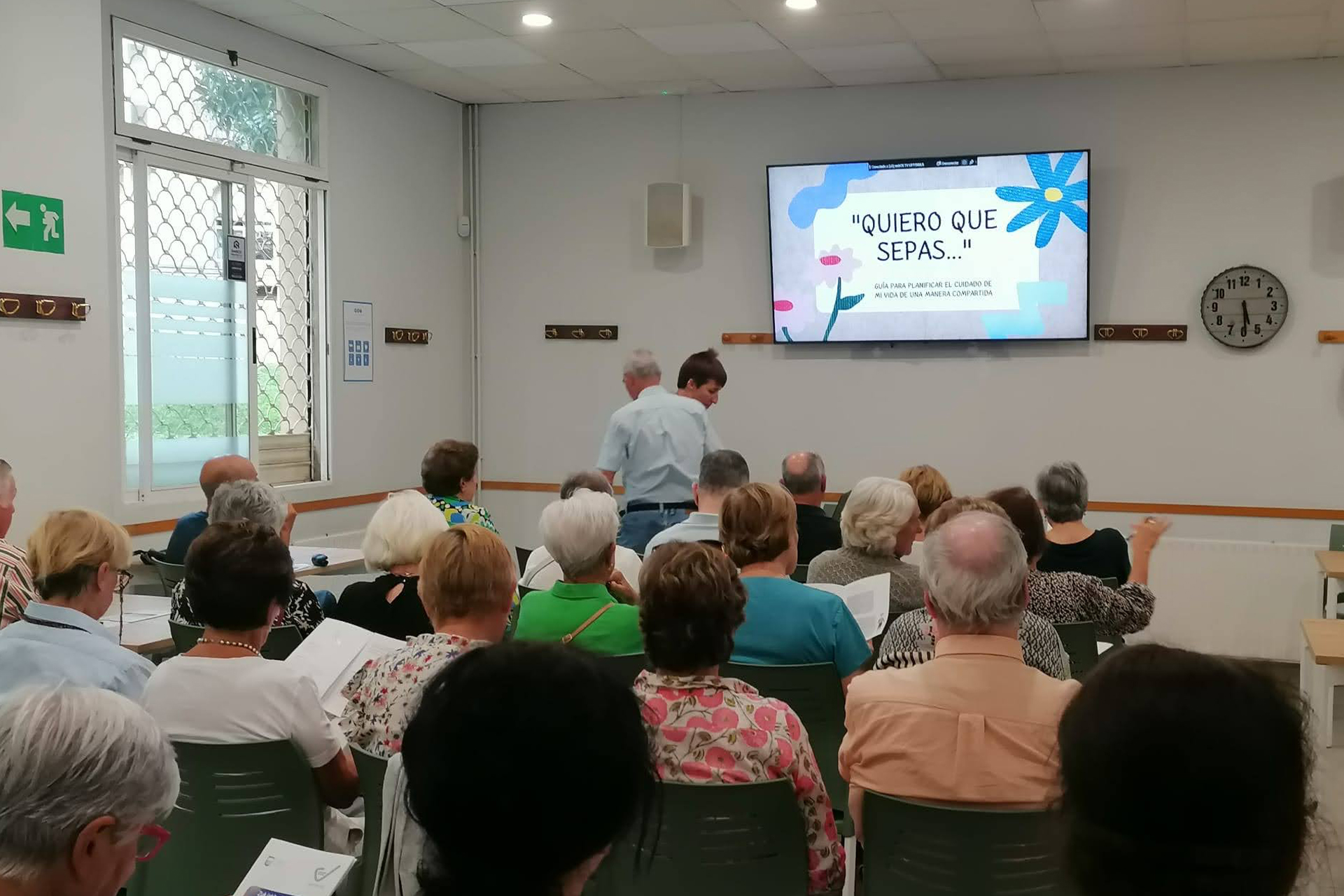 grupo de personas reunido en una sala mirando una pantalla con contenido