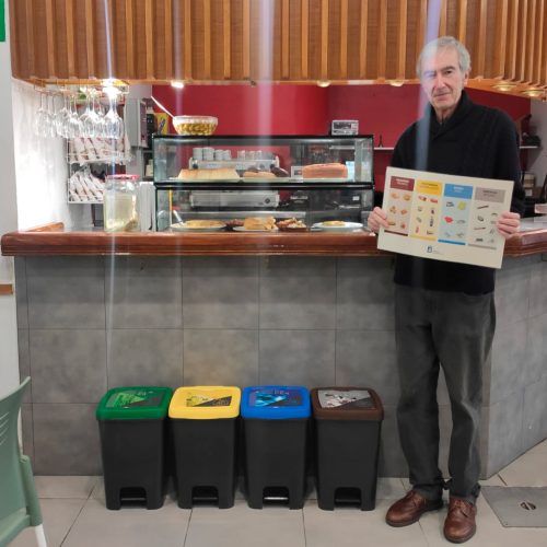 Persona sujetando un cartel con cubos de reciclaje a un lado