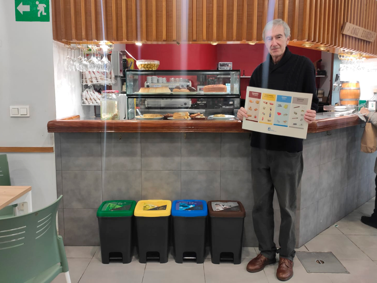 Persona sujetando un cartel con cubos de reciclaje a un lado