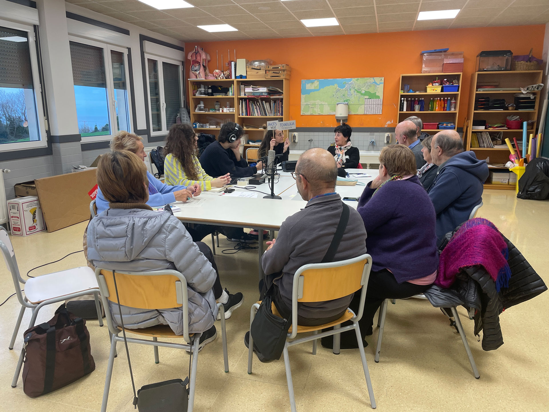 grupo de personas reunidas alrededor de una mesa, mientras un chico graba con micrófono