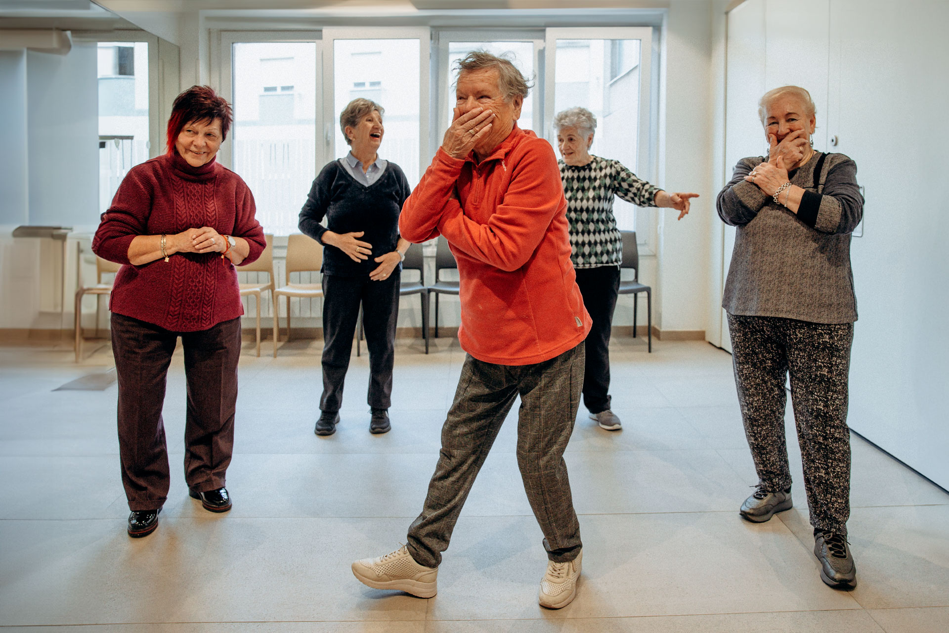 Grupo de personas realizando gestos con el cuerpo, en una sala interior
