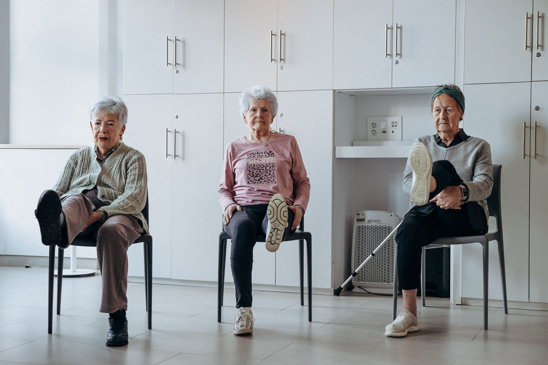 Tres personas sentadas en una silla realizando ejercicios de piernas