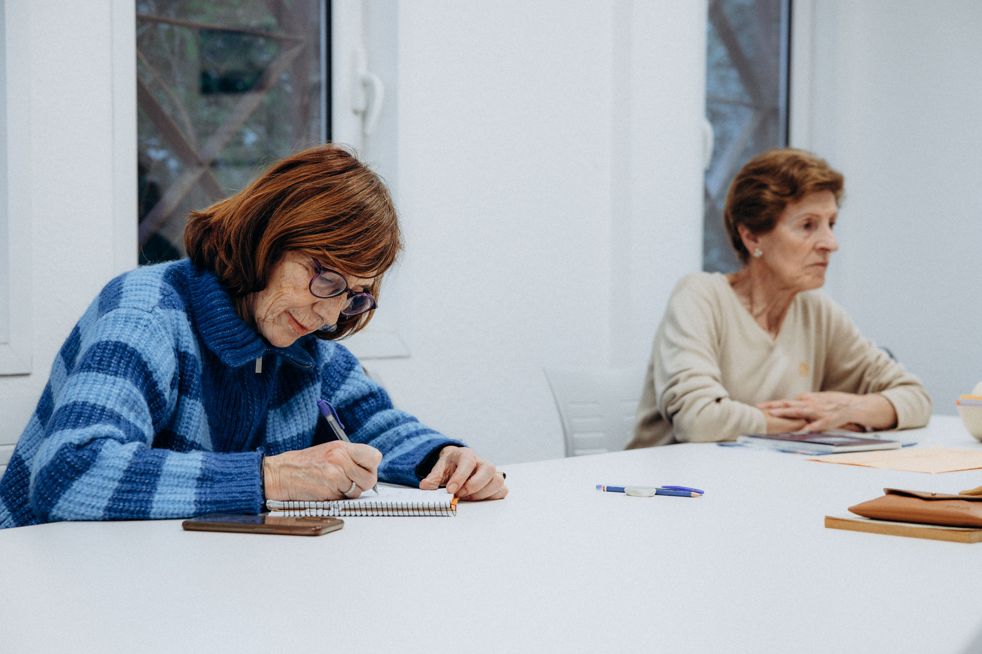 Dos personas escribiendo en un cuaderno sobre una mesa