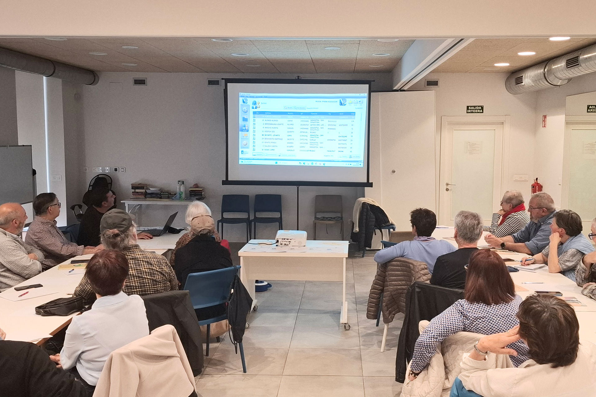 Sala llena de gente frente a una pantalla con explicaciones