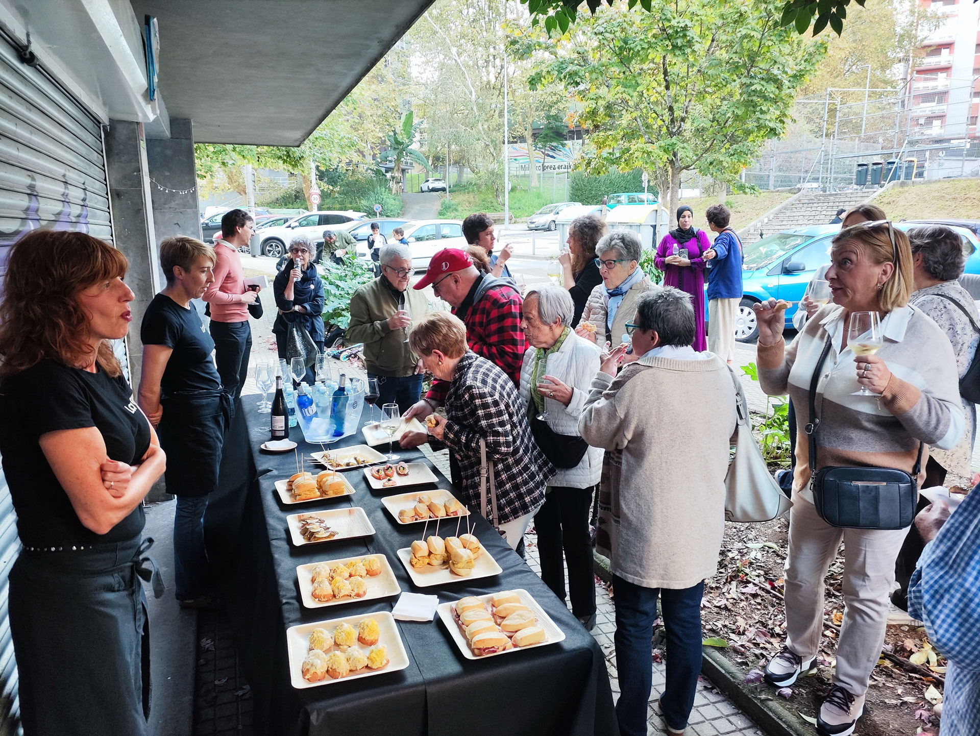 Varias personas reunidas en la calle frente a un local, comiendo unos pintxos