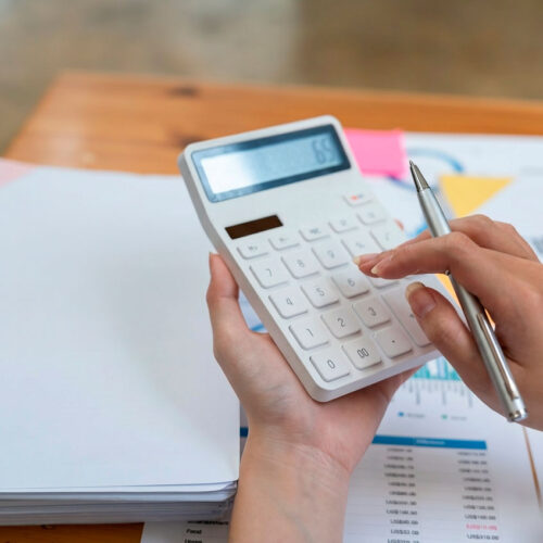 Unas manos sujetando una calculadora sobre una mesa de escritorio llena de papeles