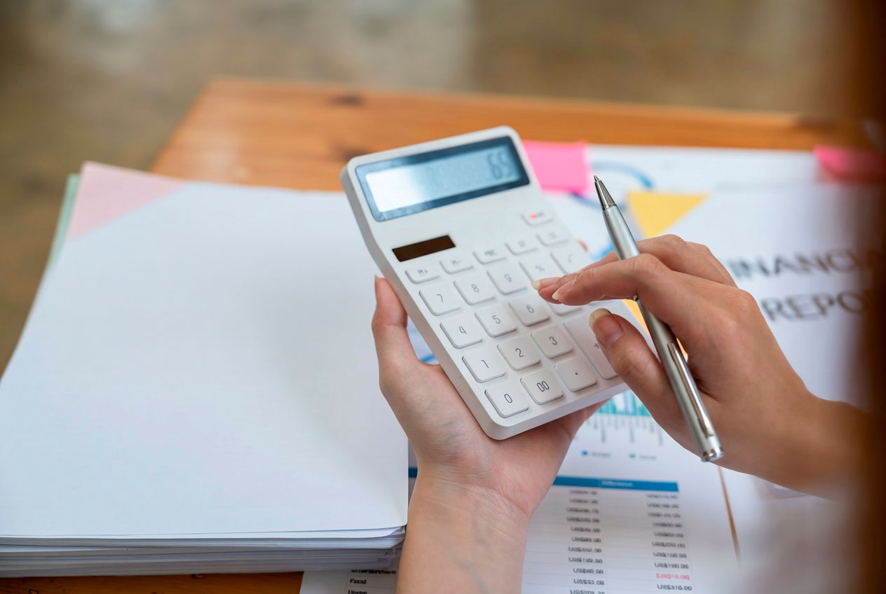 Unas manos sujetando una calculadora sobre una mesa de escritorio llena de papeles