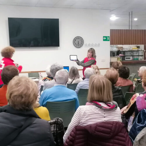 Varias personas reunidas atendiendo explicaciones de una persona que sujeta una tablet