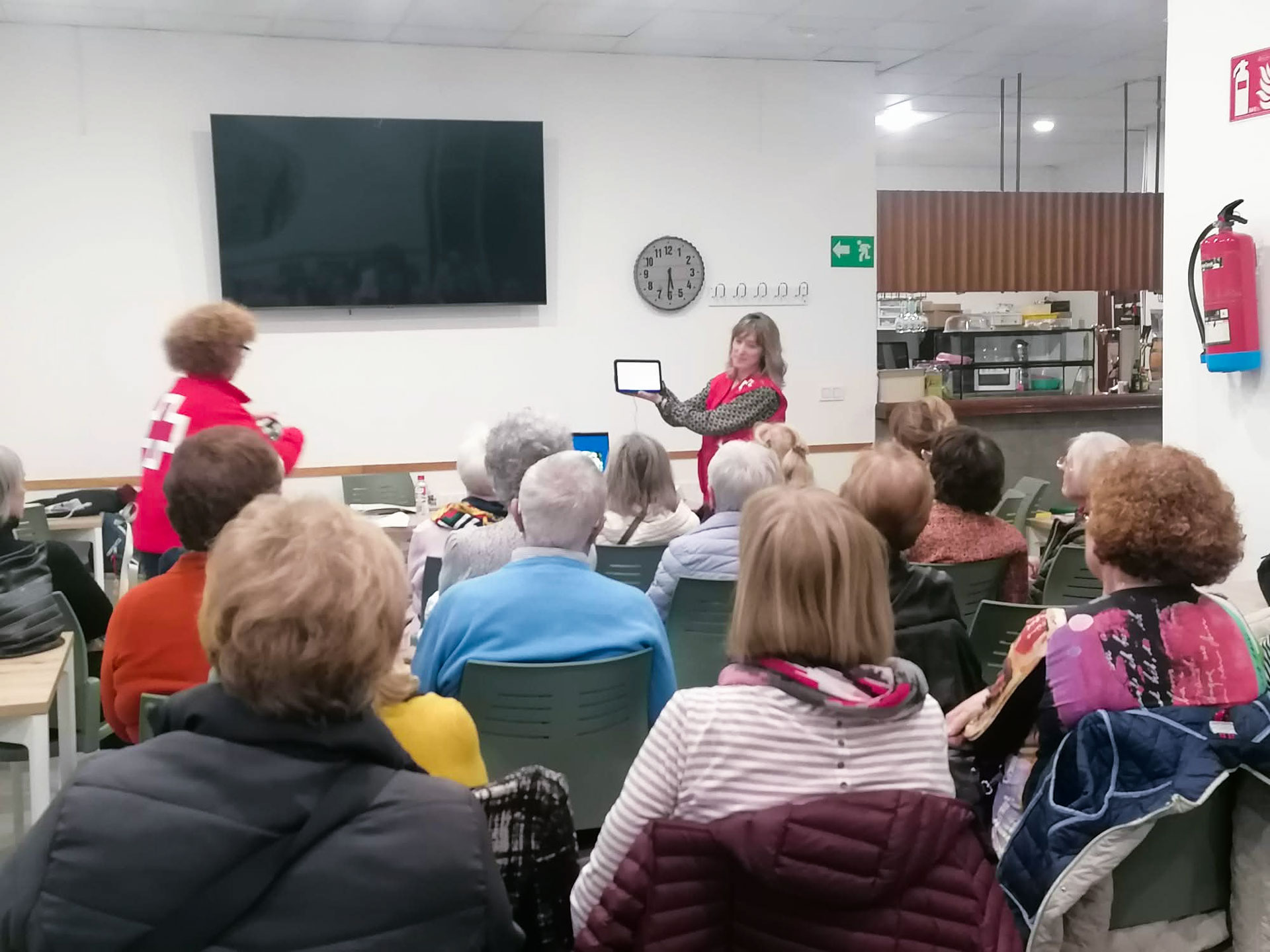 Varias personas reunidas atendiendo explicaciones de una persona que sujeta una tablet
